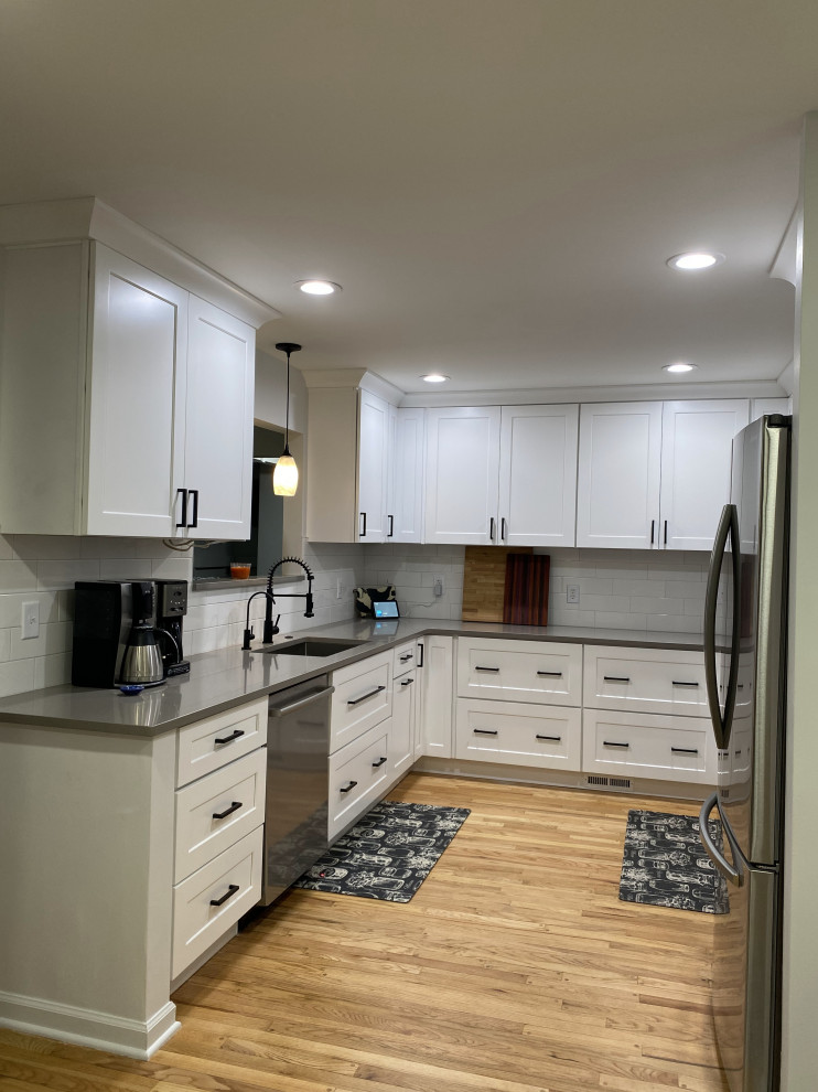 Design ideas for a mid-sized transitional galley eat-in kitchen in Detroit with an undermount sink, shaker cabinets, white cabinets, quartz benchtops, white splashback, ceramic splashback, stainless steel appliances, light hardwood floors, no island, brown floor and white benchtop.