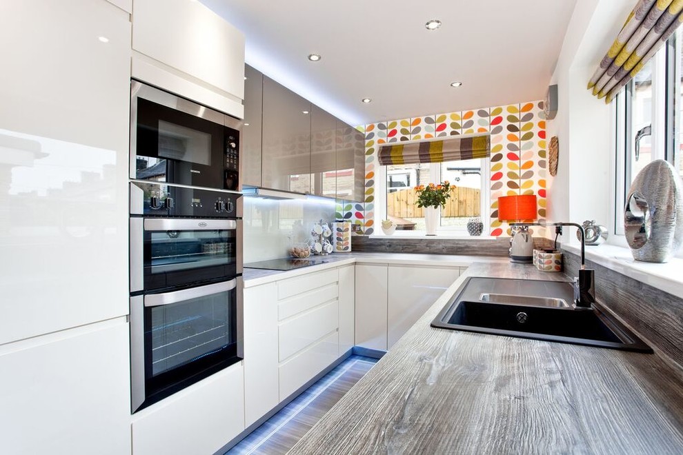 This is an example of a small modern galley eat-in kitchen in Other with a double-bowl sink, flat-panel cabinets, white cabinets, quartzite benchtops, white splashback, glass sheet splashback, stainless steel appliances, linoleum floors and a peninsula.