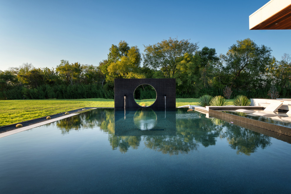 Стильный дизайн: большой прямоугольный бассейн-инфинити на заднем дворе в стиле модернизм с покрытием из каменной брусчатки - последний тренд