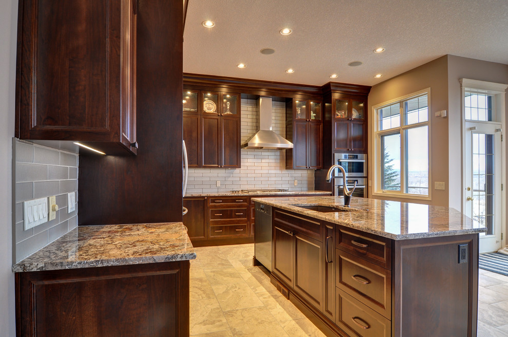 Inspiration for a large traditional u-shaped eat-in kitchen in Calgary with an undermount sink, shaker cabinets, dark wood cabinets, granite benchtops, grey splashback, glass tile splashback, stainless steel appliances, travertine floors and with island.