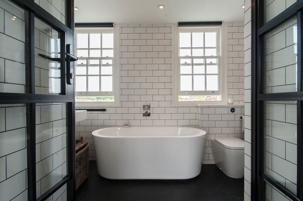 This is an example of a transitional bathroom in London with a freestanding tub, a one-piece toilet, white tile and subway tile.