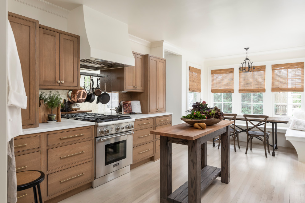 Mid-sized traditional galley separate kitchen in Chicago with a drop-in sink, beaded inset cabinets, medium wood cabinets, marble benchtops, metallic splashback, mirror splashback, stainless steel appliances, light hardwood floors, with island, brown floor and white benchtop.