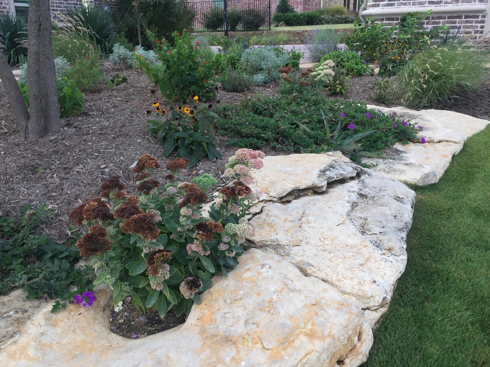 This is an example of a large country front yard full sun xeriscape in Dallas with a retaining wall and natural stone pavers.