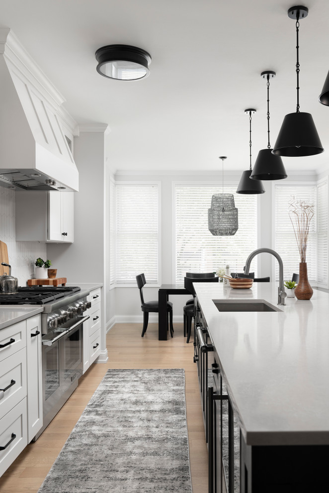 Inspiration for a mid-sized transitional galley light wood floor open concept kitchen remodel in Chicago with an undermount sink, shaker cabinets, white cabinets, quartz countertops, white backsplash, ceramic backsplash, stainless steel appliances, an island and gray countertops