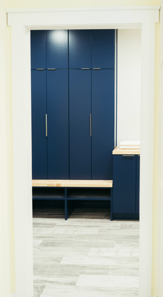 Inspiration for a large modern u-shaped utility room in Other with shaker cabinets, blue splashback, glass tile splashback, porcelain floors, grey floor, blue cabinets, a single-bowl sink, wood benchtops, yellow walls, a side-by-side washer and dryer and brown benchtop.