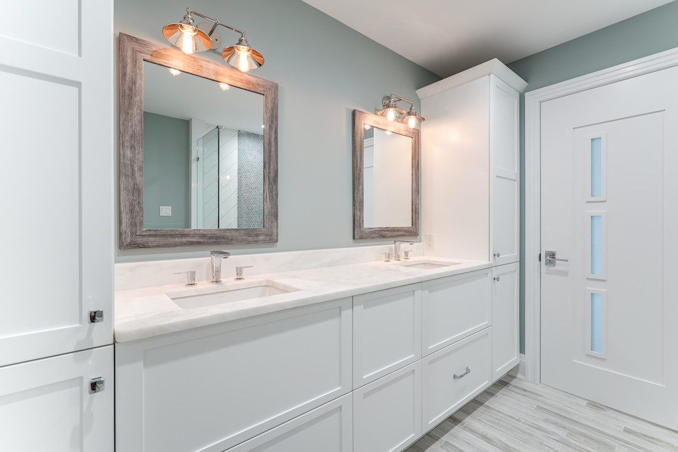 Inspiration for a mid-sized transitional master bathroom in Philadelphia with recessed-panel cabinets, white cabinets, a corner shower, white tile, porcelain tile, blue walls, light hardwood floors, an undermount sink, marble benchtops, beige floor and a hinged shower door.