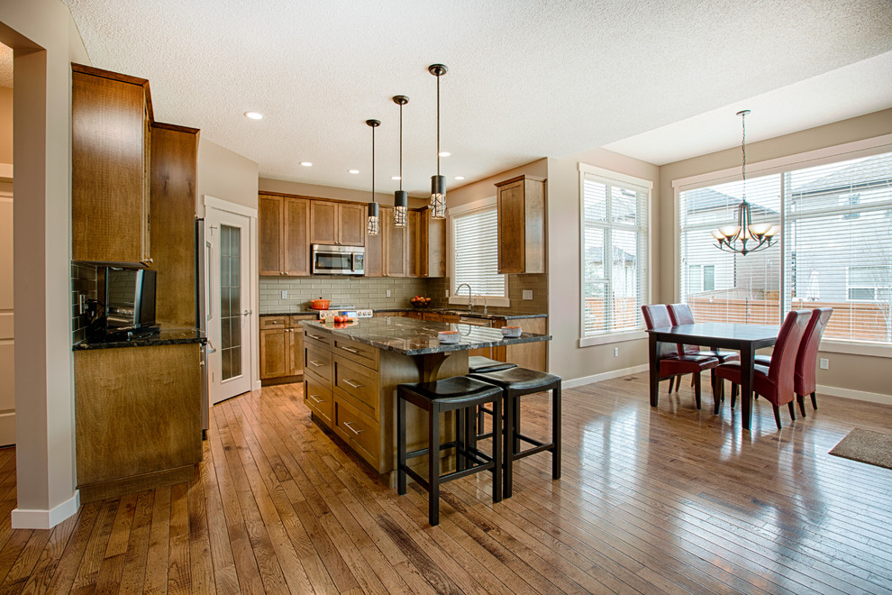 Inspiration for a mid-sized rustic u-shaped medium tone wood floor and brown floor eat-in kitchen remodel in Calgary with an undermount sink, shaker cabinets, medium tone wood cabinets, granite countertops, gray backsplash, glass tile backsplash, stainless steel appliances and an island