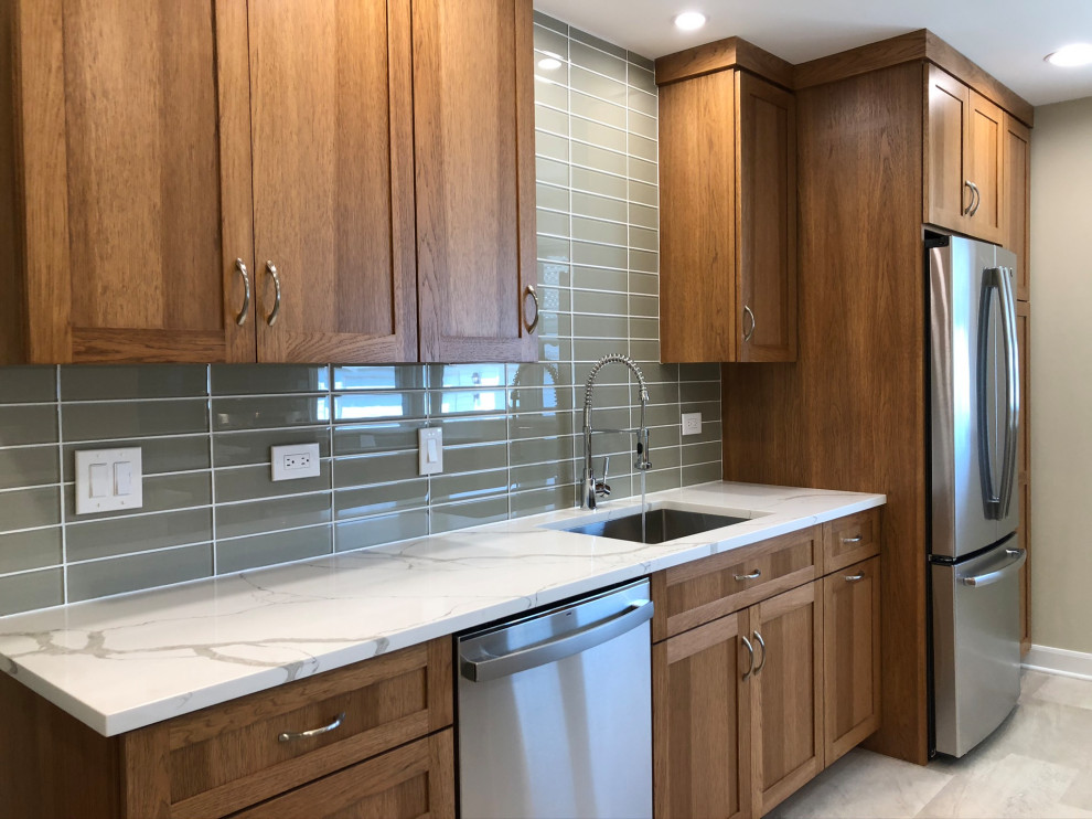 Photo of a small transitional eat-in kitchen in Chicago with a single-bowl sink, flat-panel cabinets, medium wood cabinets, quartz benchtops, green splashback, glass tile splashback, stainless steel appliances, no island, grey floor and white benchtop.