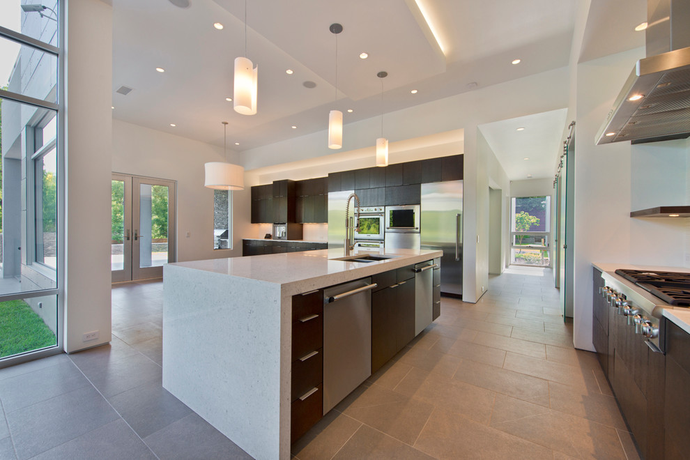 Large l-shaped porcelain tile open concept kitchen photo with a double-bowl sink, flat-panel cabinets, dark wood cabinets, quartz countertops, white backsplash, porcelain backsplash, stainless steel appliances and an island