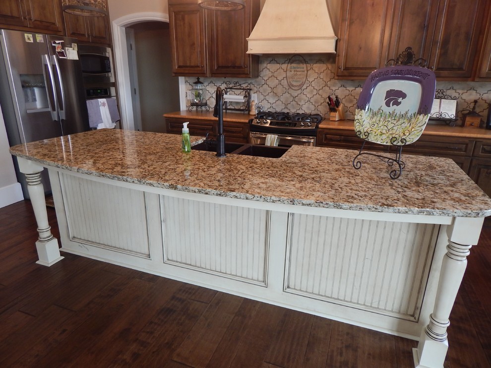 Mid-sized elegant single-wall dark wood floor and brown floor enclosed kitchen photo with an undermount sink, raised-panel cabinets, dark wood cabinets, granite countertops, beige backsplash, porcelain backsplash, stainless steel appliances and an island