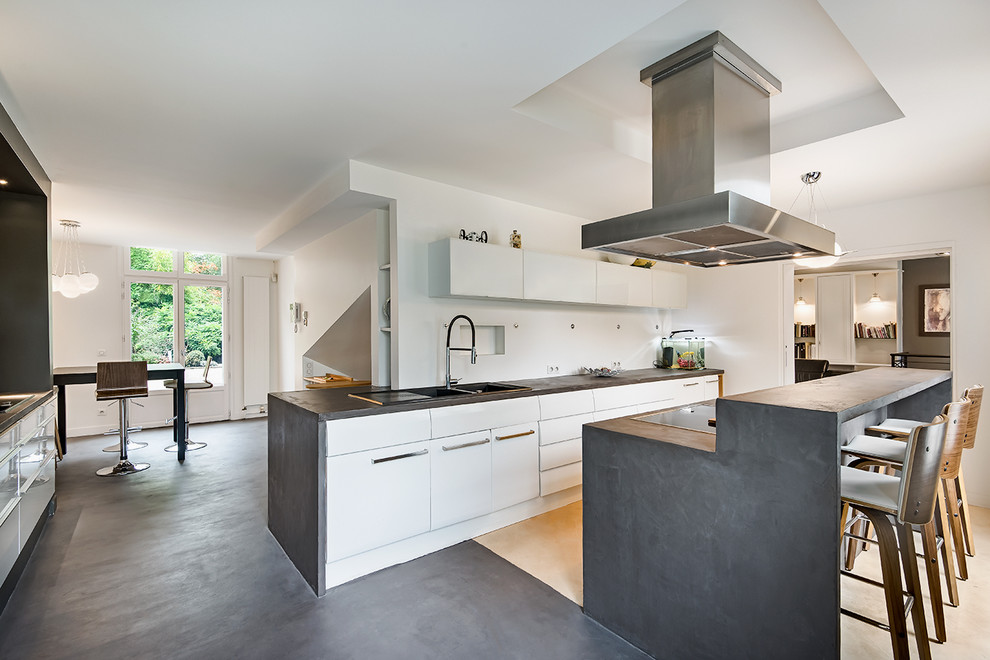 Design ideas for a large contemporary l-shaped open plan kitchen in Paris with white cabinets, concrete benchtops, white splashback, concrete floors, with island, an integrated sink, flat-panel cabinets and white appliances.