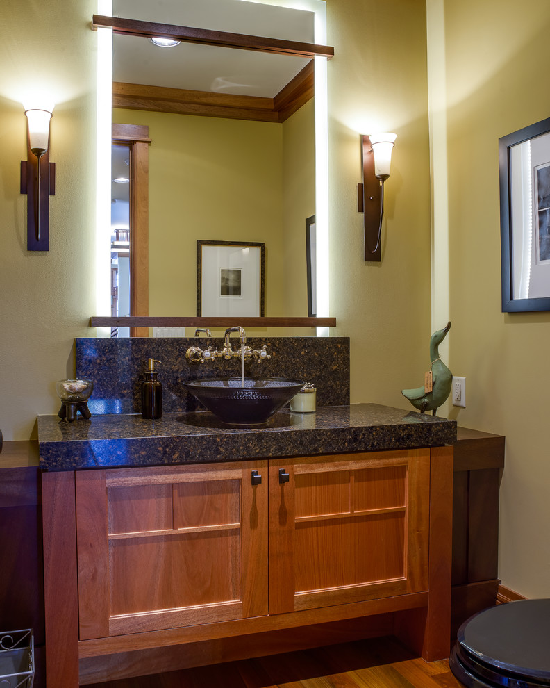 Arts and crafts powder room in Minneapolis with a vessel sink, recessed-panel cabinets, medium wood cabinets, beige walls and black benchtops.