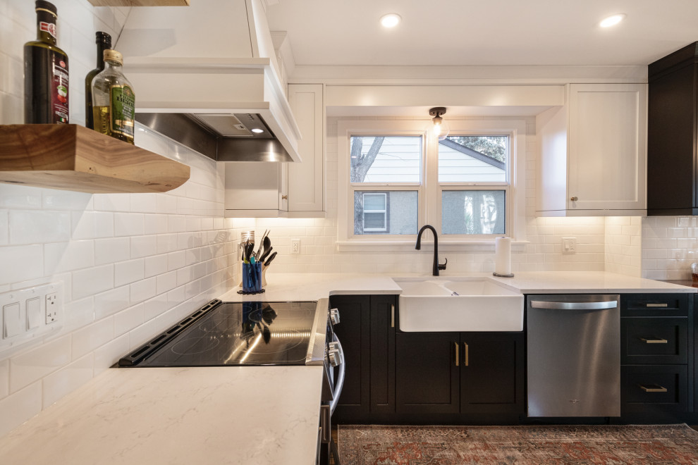 This is an example of a medium sized country u-shaped kitchen/diner in Edmonton with a belfast sink, recessed-panel cabinets, black cabinets, engineered stone countertops, white splashback, ceramic splashback, stainless steel appliances, no island, brown floors, white worktops and dark hardwood flooring.