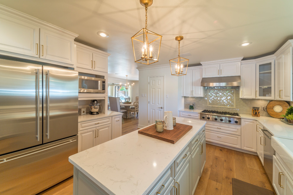 Enclosed kitchen - large transitional u-shaped medium tone wood floor and brown floor enclosed kitchen idea with a farmhouse sink, raised-panel cabinets, white cabinets, quartz countertops, gray backsplash, glass tile backsplash, stainless steel appliances and an island
