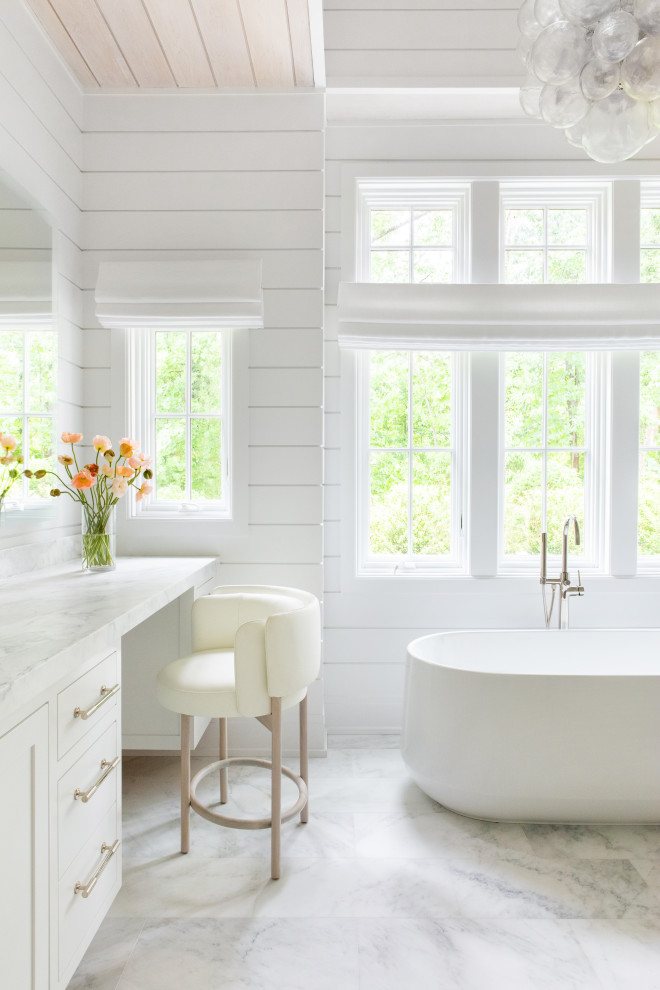 Design ideas for an expansive transitional master bathroom in New York with beaded inset cabinets, white cabinets, a freestanding tub, an alcove shower, white walls, marble floors, an integrated sink, marble benchtops, white floor, a hinged shower door, white benchtops, a double vanity, a built-in vanity, vaulted and panelled walls.