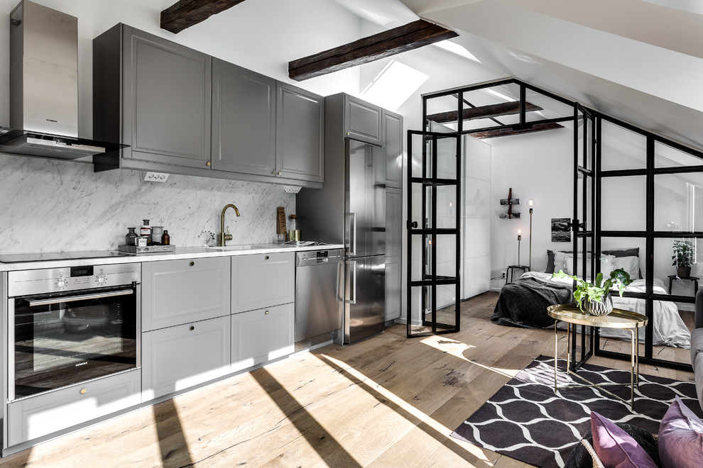 Design ideas for a mid-sized industrial single-wall open plan kitchen in Stockholm with raised-panel cabinets, grey cabinets, grey splashback, stainless steel appliances, light hardwood floors and no island.
