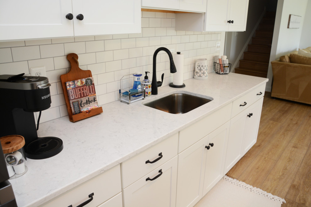 Bild på ett litet vintage vit linjärt vitt kök med öppen planlösning, med en undermonterad diskho, luckor med infälld panel, vita skåp, bänkskiva i kvarts, vitt stänkskydd, rostfria vitvaror, mellanmörkt trägolv, en köksö och brunt golv