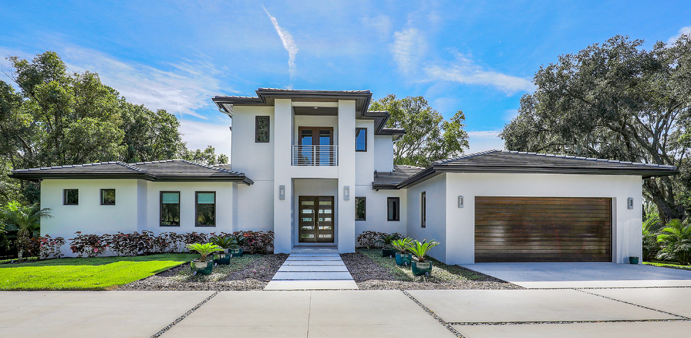 Photo of an expansive contemporary two-storey stucco white house exterior in Tampa with a hip roof and a shingle roof.