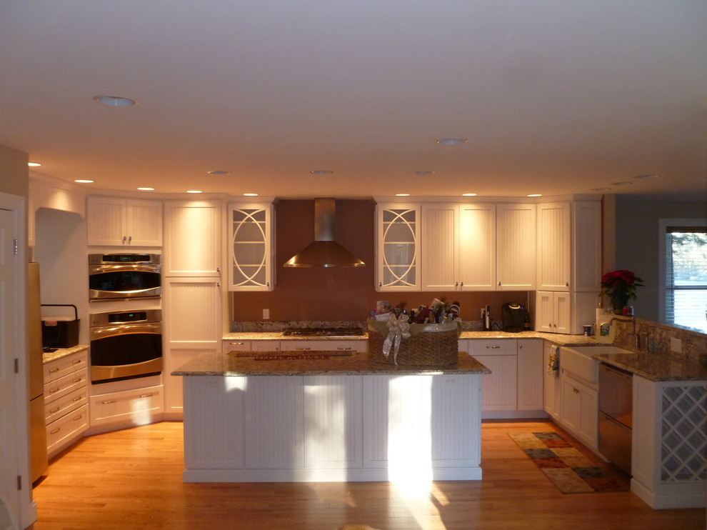 Kitchen - large traditional u-shaped light wood floor kitchen idea in Boston with a farmhouse sink, white cabinets, granite countertops, stainless steel appliances and an island