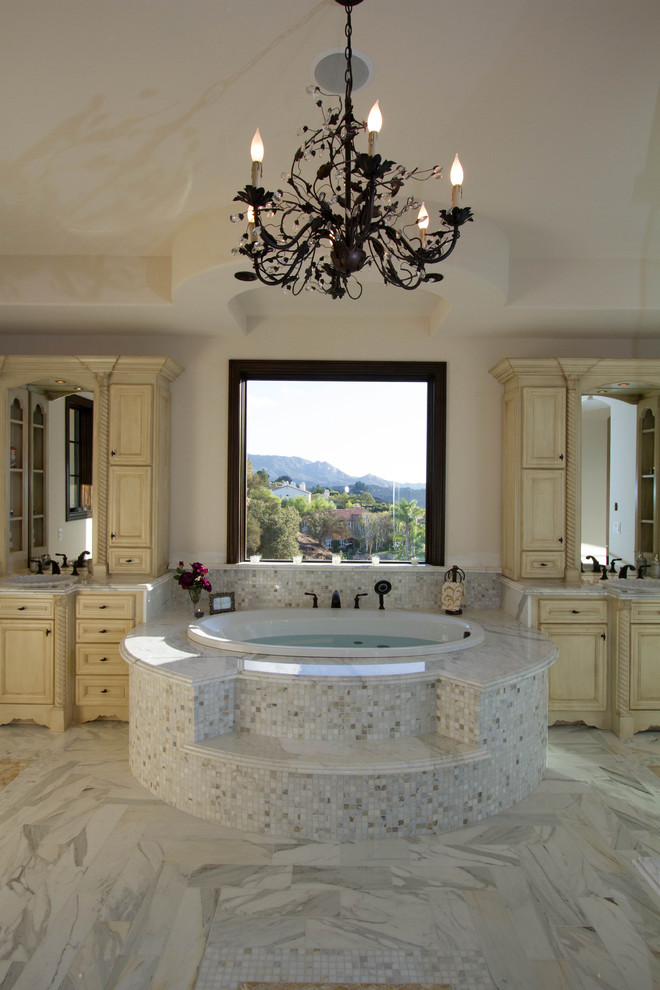 Photo of a mediterranean bathroom in Los Angeles with beige cabinets, a drop-in tub, white tile and stone tile.