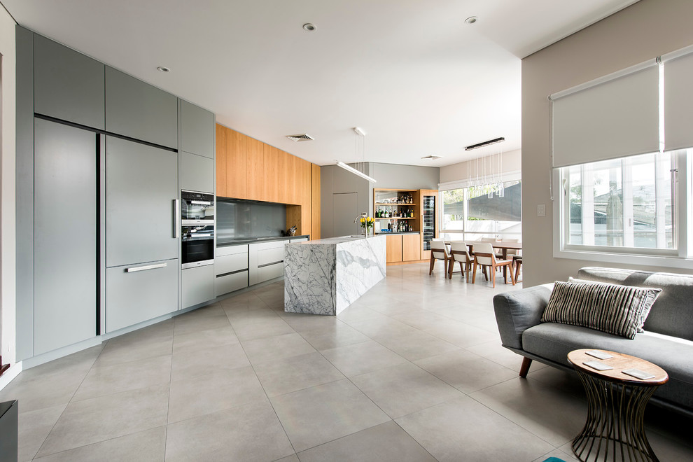 Inspiration for a mid-sized contemporary single-wall open plan kitchen in Perth with a drop-in sink, recessed-panel cabinets, grey cabinets, solid surface benchtops, grey splashback, glass sheet splashback, stainless steel appliances, porcelain floors and with island.