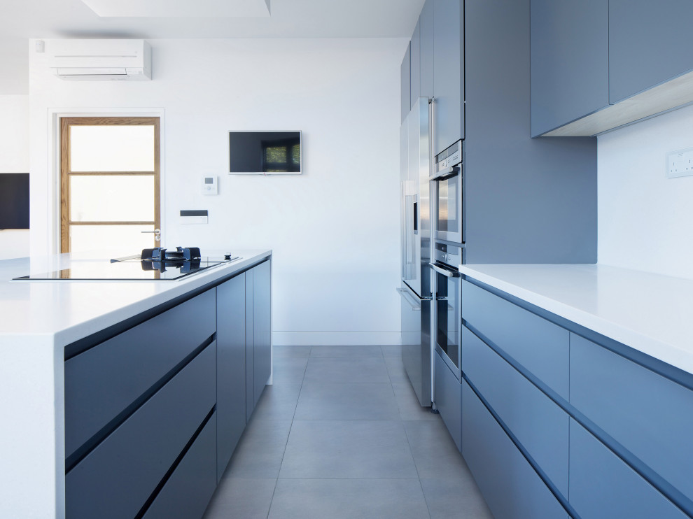 Photo of a mid-sized modern l-shaped open plan kitchen in London with a drop-in sink, recessed-panel cabinets, grey cabinets, quartz benchtops, white splashback, black appliances, cement tiles, with island, grey floor and white benchtop.