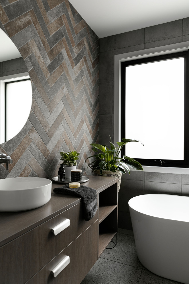 Mid-sized contemporary master bathroom in Melbourne with flat-panel cabinets, medium wood cabinets, a freestanding tub, brown tile, gray tile, a vessel sink, wood benchtops, grey floor, brown benchtops, a single vanity and a freestanding vanity.