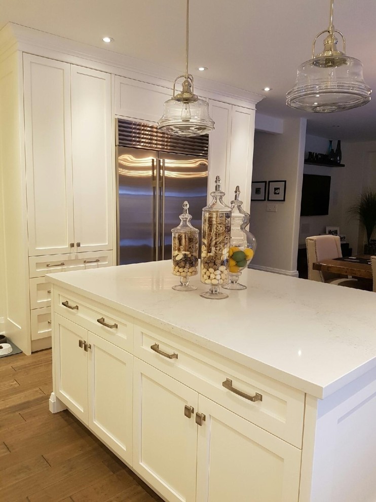 Inspiration for a mid-sized transitional l-shaped medium tone wood floor and brown floor open concept kitchen remodel in Toronto with an undermount sink, beaded inset cabinets, white cabinets, solid surface countertops, white backsplash, brick backsplash, stainless steel appliances, an island and white countertops