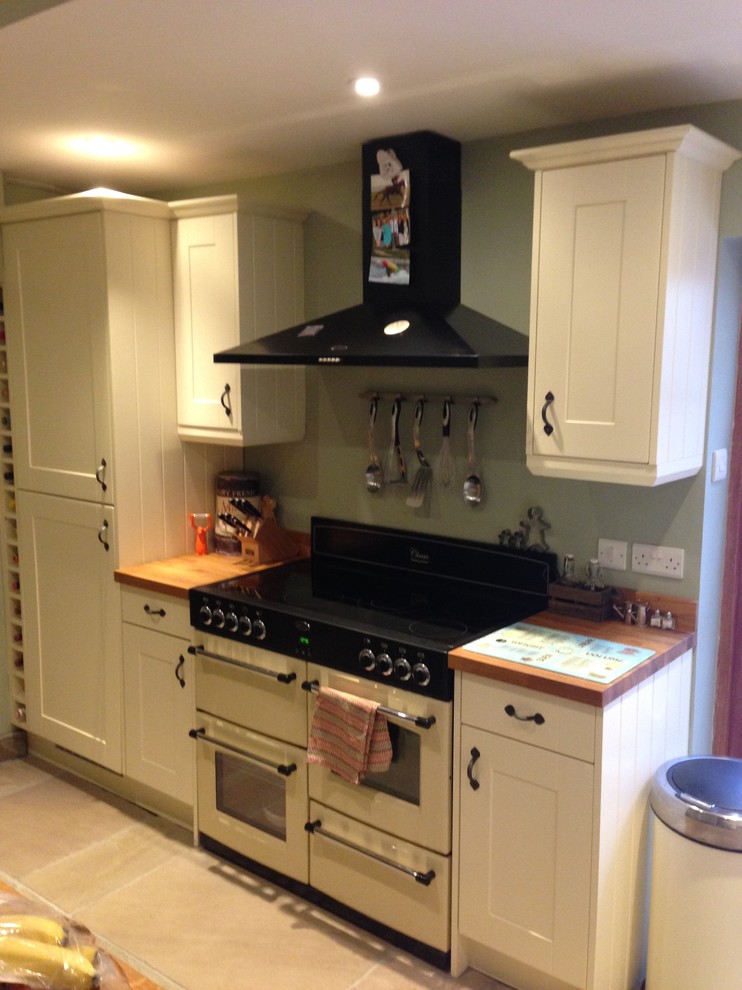 Design ideas for a small traditional l-shaped eat-in kitchen in Cambridgeshire with a drop-in sink, shaker cabinets, beige cabinets, wood benchtops, multi-coloured splashback, glass sheet splashback, black appliances and travertine floors.