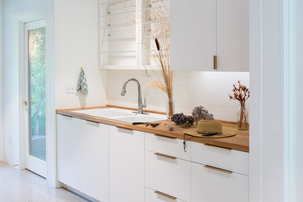 Photo of a modern galley utility room in Portland with a drop-in sink, flat-panel cabinets, white cabinets, wood benchtops, white splashback, shiplap splashback, white walls, concrete floors, grey floor, brown benchtop and planked wall panelling.
