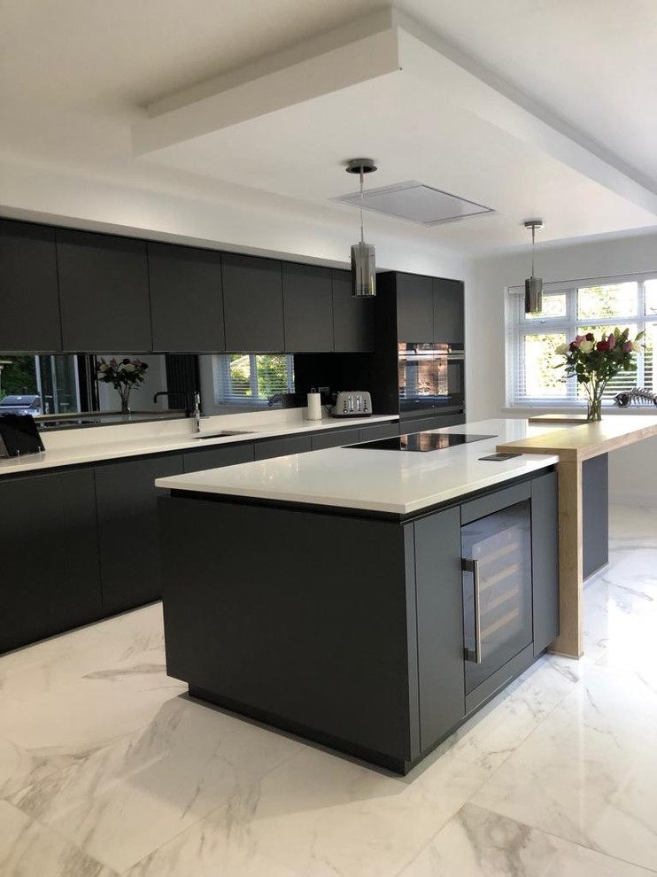 Photo of a large modern galley open plan kitchen in Manchester with flat-panel cabinets, black cabinets, metallic splashback, glass tile splashback, stainless steel appliances, porcelain floors, with island, white floor and white benchtop.