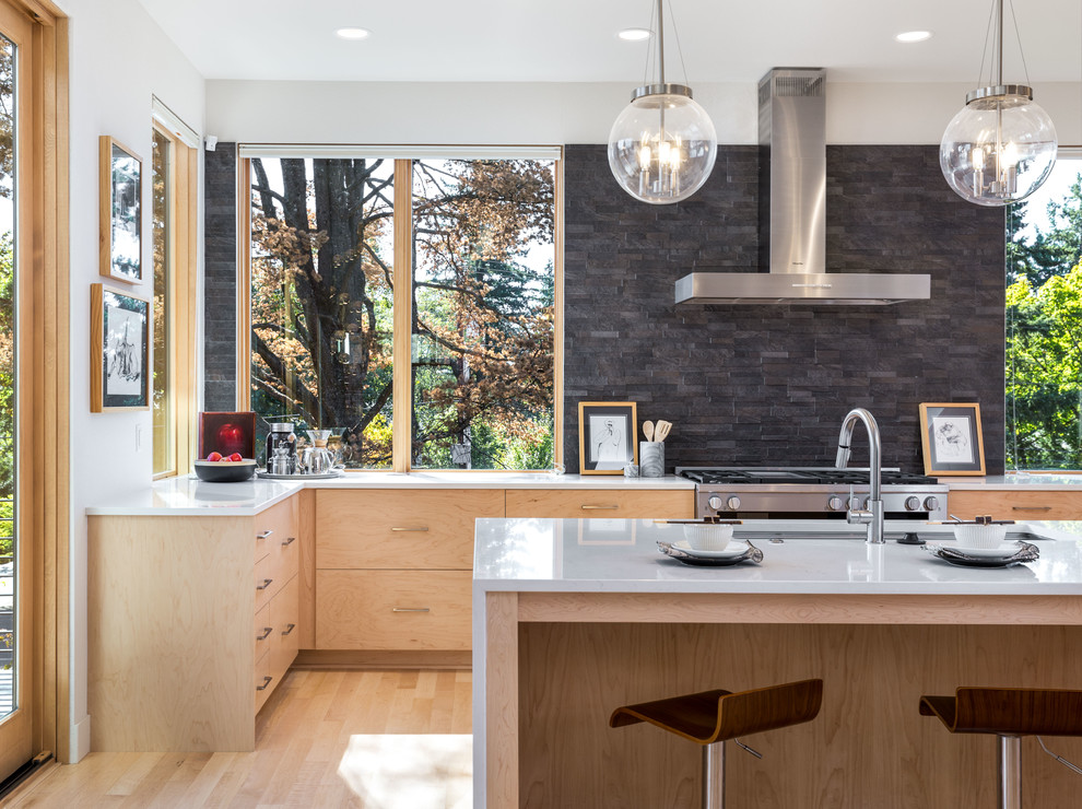 This is an example of a contemporary kitchen in Portland with flat-panel cabinets, light wood cabinets, black splashback, stone tile splashback, light hardwood floors, with island and beige floor.
