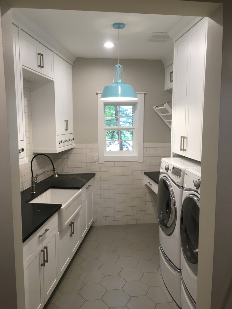 This is an example of a large contemporary utility room in Boise with a farmhouse sink, white cabinets, granite benchtops, porcelain floors and a side-by-side washer and dryer.