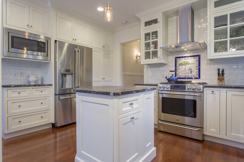 Klassische Küche mit Landhausspüle, Kassettenfronten, weißen Schränken, Granit-Arbeitsplatte, Elektrogeräten mit Frontblende und Kücheninsel in Providence