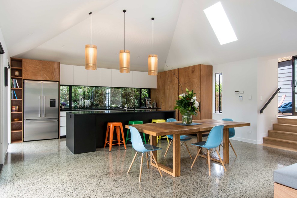 Photo of a large modern l-shaped eat-in kitchen in Auckland with granite benchtops, window splashback, stainless steel appliances, concrete floors, with island and black benchtop.