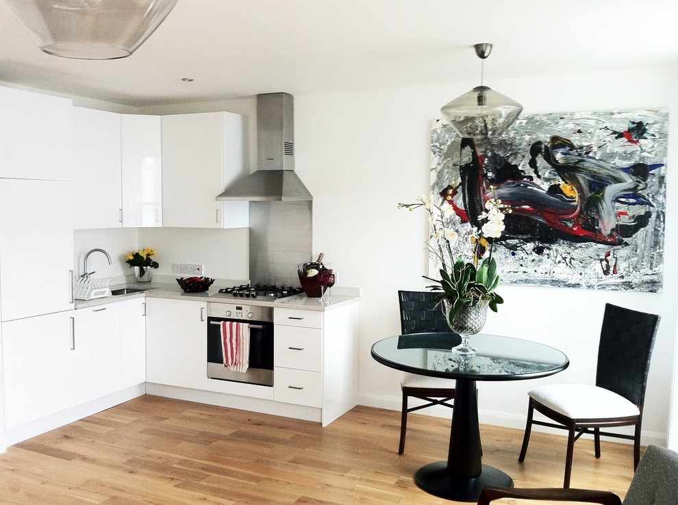 Contemporary l-shaped eat-in kitchen in London with an undermount sink, flat-panel cabinets and white cabinets.