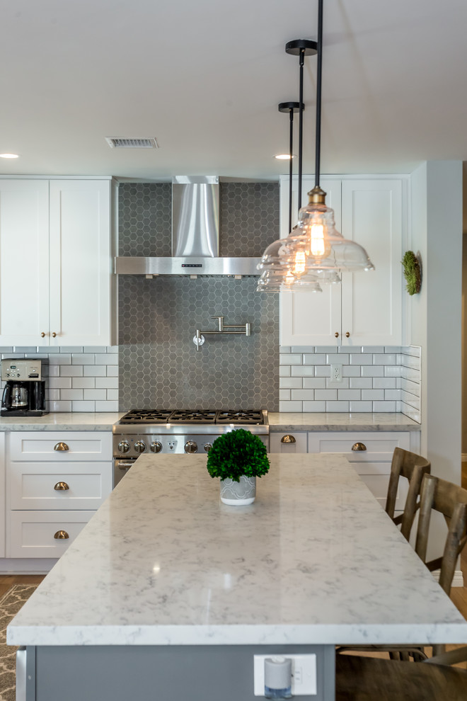 Photo of a large traditional l-shaped eat-in kitchen in Los Angeles with a farmhouse sink, shaker cabinets, white cabinets, marble benchtops, white splashback, subway tile splashback, stainless steel appliances, medium hardwood floors, with island, brown floor and grey benchtop.