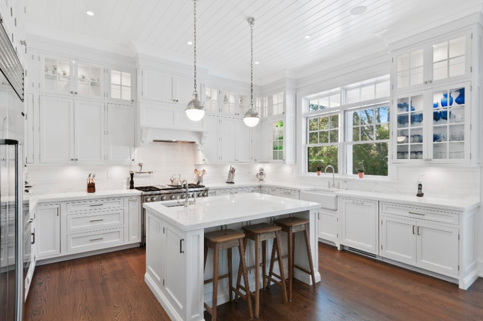 Inspiration for a large traditional u-shaped eat-in kitchen in New York with a farmhouse sink, recessed-panel cabinets, white cabinets, marble benchtops, white splashback, marble splashback, stainless steel appliances, medium hardwood floors, with island, brown floor, white benchtop and timber.