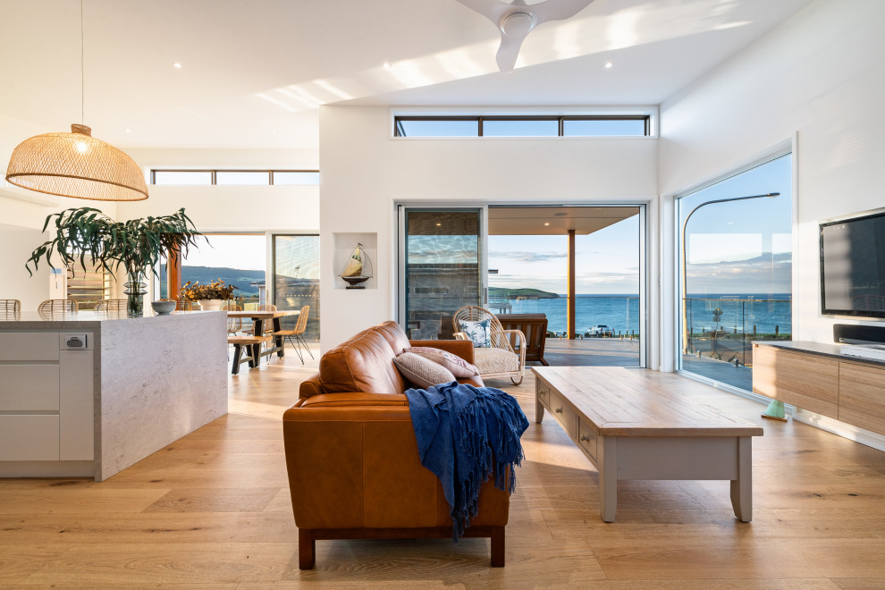 Photo of a large beach style open concept living room in Wollongong with white walls, medium hardwood floors, a wall-mounted tv and brown floor.