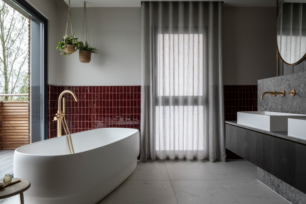 Пример оригинального дизайна: ванная комната в современном стиле с плоскими фасадами, темными деревянными фасадами, отдельно стоящей ванной, красной плиткой, серыми стенами, настольной раковиной, серым полом, серой столешницей, тумбой под две раковины и подвесной тумбой