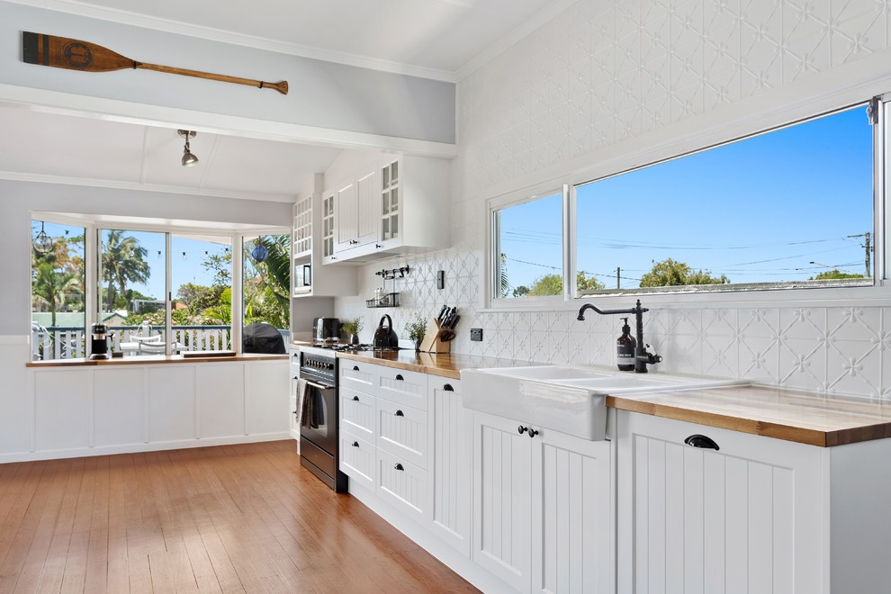 Inspiration for a transitional single-wall kitchen in Gold Coast - Tweed with a farmhouse sink, shaker cabinets, white cabinets, white splashback, black appliances and medium hardwood floors.