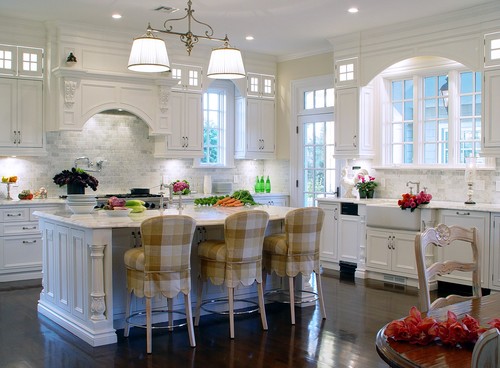 Bright, elegant kitchen with white shaker-style cabinets, marble countertops, a large island with three upholstered stools, pendant lights, and a farmhouse sink by tall windows—Kitchen Cabinet Mississauga.