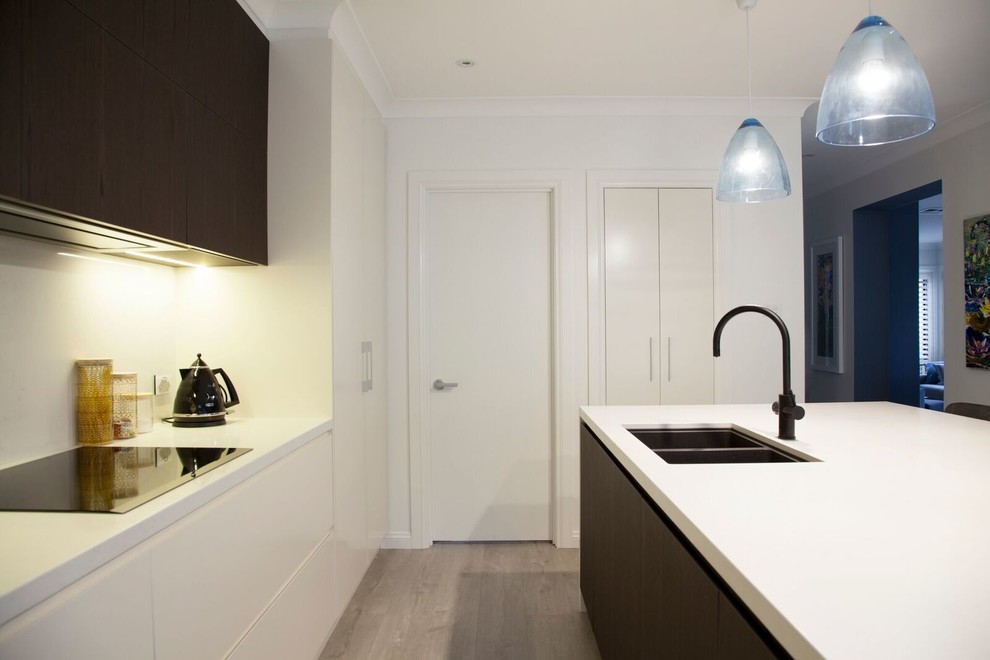 Photo of a mid-sized contemporary galley open plan kitchen in Sydney with a double-bowl sink, flat-panel cabinets, white cabinets, quartz benchtops, white splashback, stone slab splashback, black appliances, light hardwood floors and with island.