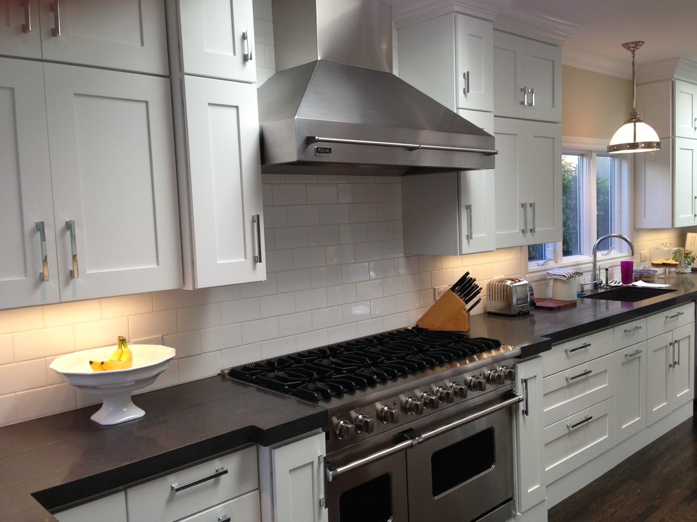 Photo of a large contemporary u-shaped eat-in kitchen in New York with a single-bowl sink, shaker cabinets, white cabinets, copper benchtops, white splashback, subway tile splashback, stainless steel appliances, painted wood floors, no island, brown floor and black benchtop.