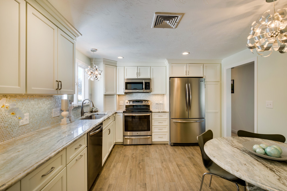 This is an example of a mid-sized transitional l-shaped eat-in kitchen in Boston with white cabinets, an undermount sink, recessed-panel cabinets, quartzite benchtops, green splashback, ceramic splashback, stainless steel appliances, ceramic floors, no island, brown floor and beige benchtop.