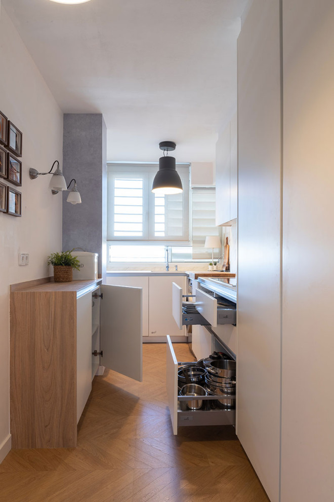 Modelo de cocina moderna pequeña con armarios con paneles lisos, puertas de armario blancas, encimera de madera, electrodomésticos de acero inoxidable y encimeras beige