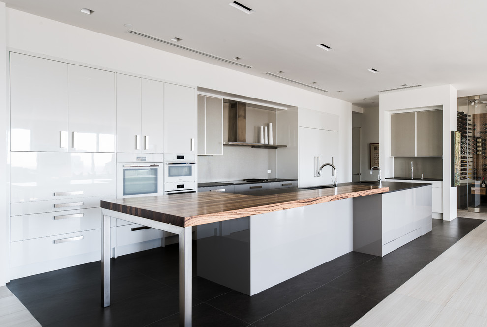 Large contemporary kitchen in Dallas with flat-panel cabinets, white cabinets, grey splashback, white appliances, porcelain floors, with island, a single-bowl sink, wood benchtops and black floor.