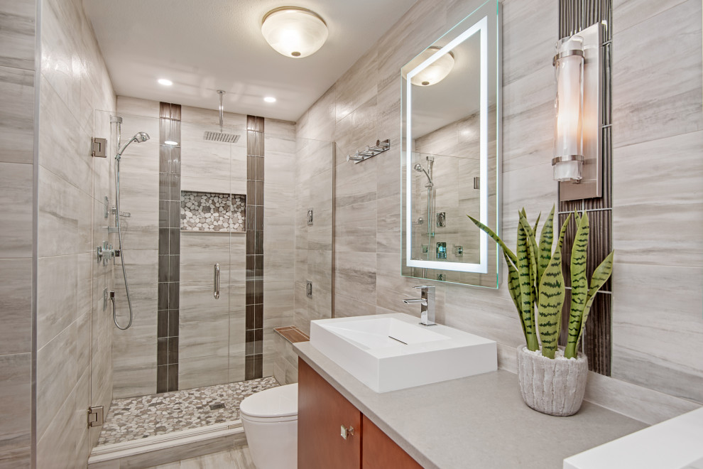 Inspiration for a mid-sized modern master bathroom in Tampa with flat-panel cabinets, medium wood cabinets, a one-piece toilet, gray tile, ceramic tile, grey walls, ceramic floors, a vessel sink, engineered quartz benchtops, grey floor, a hinged shower door and grey benchtops.
