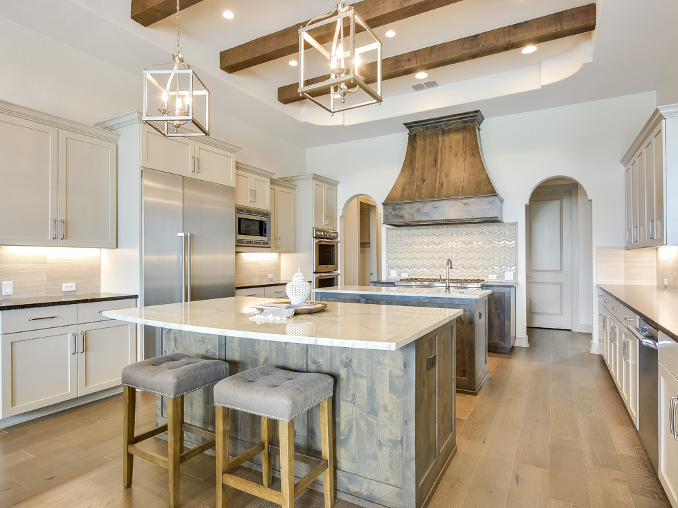 This is an example of a mediterranean separate kitchen in Austin with shaker cabinets, beige cabinets, multiple islands, metallic splashback, stainless steel appliances and medium hardwood floors.