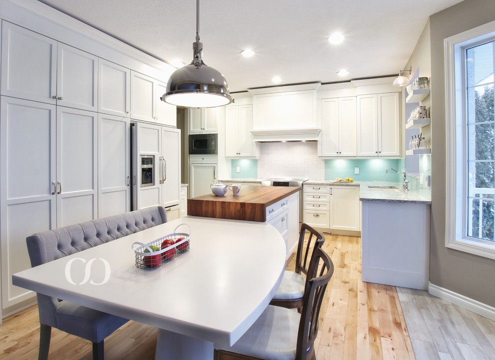 Inspiration for a mid-sized transitional l-shaped light wood floor open concept kitchen remodel with an undermount sink, recessed-panel cabinets, white cabinets, quartz countertops, blue backsplash, glass sheet backsplash, paneled appliances and an island